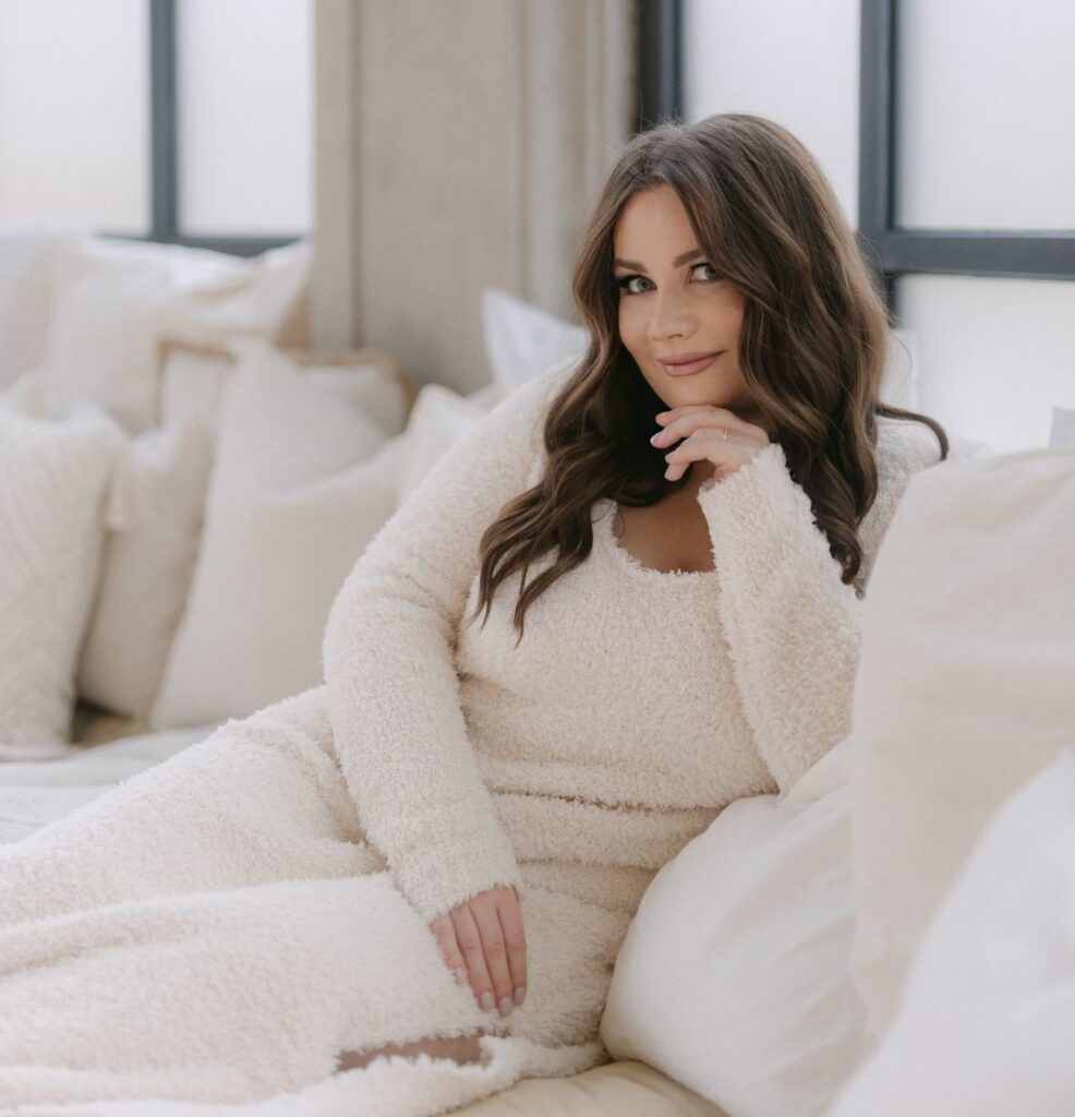 Anna sitzt entspannt in beiger Loungewear auf einem Sofa und blickt zur Seite
